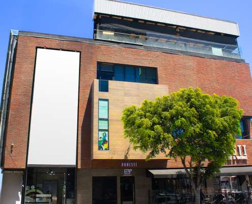 Brick urban building with a tall blank white billboard on the left and a green tree in front, street-level shops below.