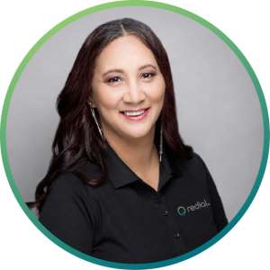 Shoana@0.5x-80 Professional headshot of a smiling woman with long dark hair, wearing a black polo shirt with a small company logo on the left chest, against a gray background and circular green-teal frame.